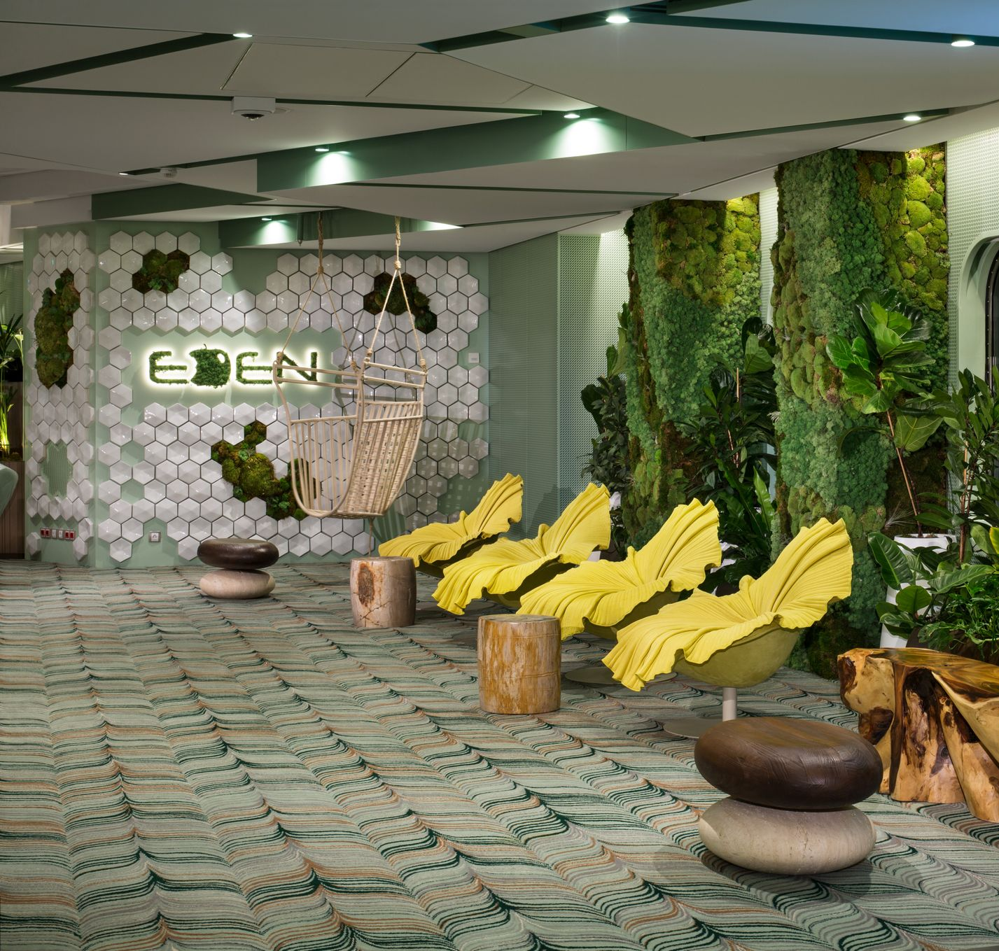 Lounge area with moss walls, yellow chairs, and wooden furniture. Sign reads 