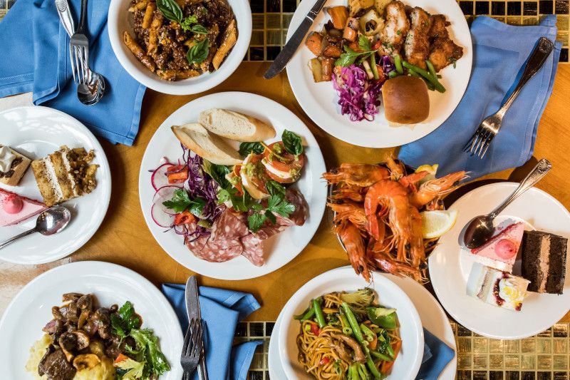 Overhead shot of a table set with various dishes: pasta, meats, vegetables, bread, and shrimp.
