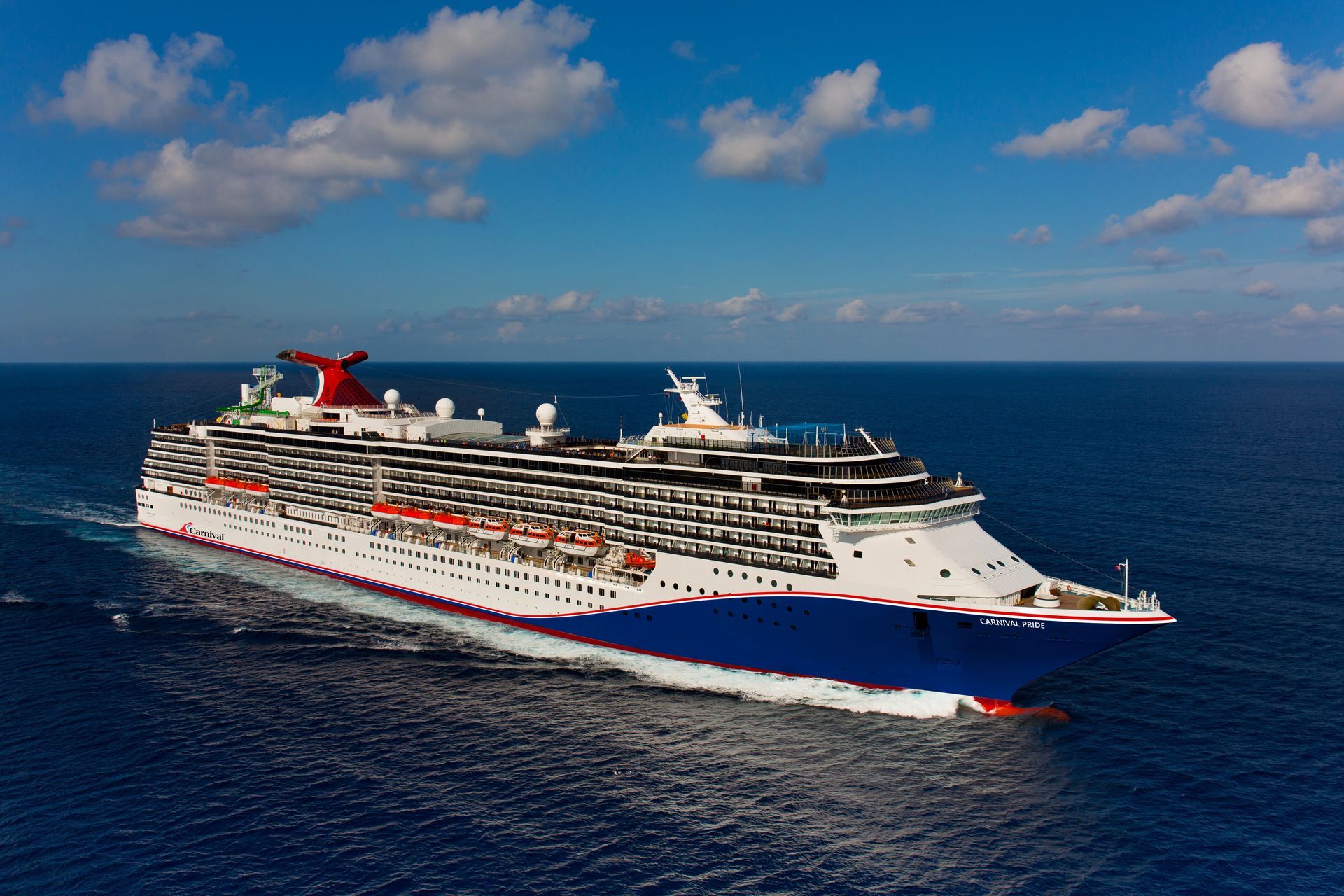 Large white cruise ship with a red-and-blue hull sailing on a calm blue ocean under a partly cloudy sky