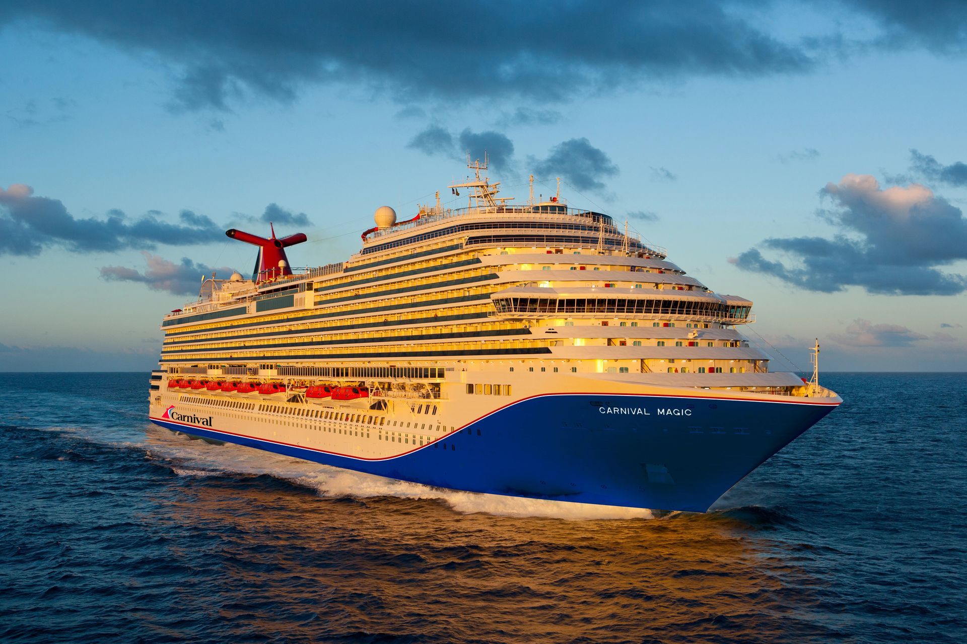 Cruise ship sailing on blue ocean under a cloudy sky. Red, white, and blue colors on the hull.