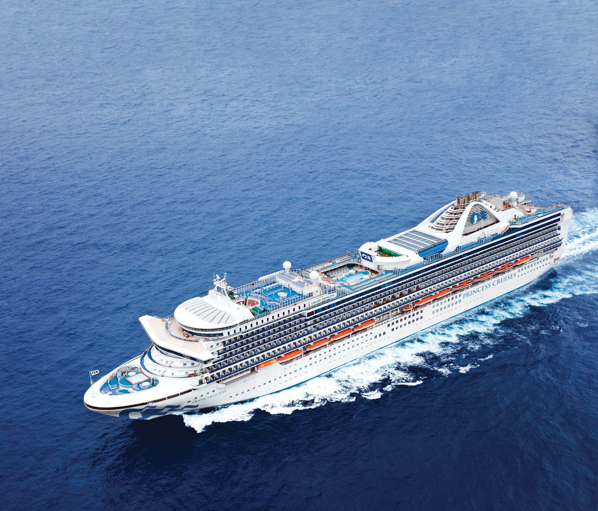 Large cruise ship sailing on blue ocean, generating a white wake.