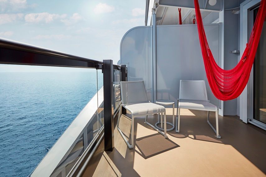 Balcony with ocean view, two white chairs, red hammock, sunny day on a cruise ship.
