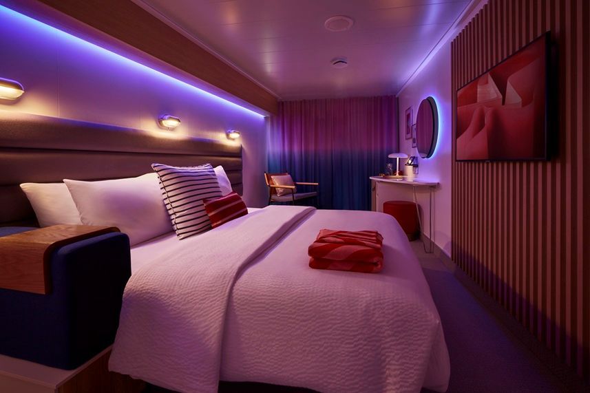 Bedroom with a king-size bed, purple and red lighting, wooden paneling, and modern decor.