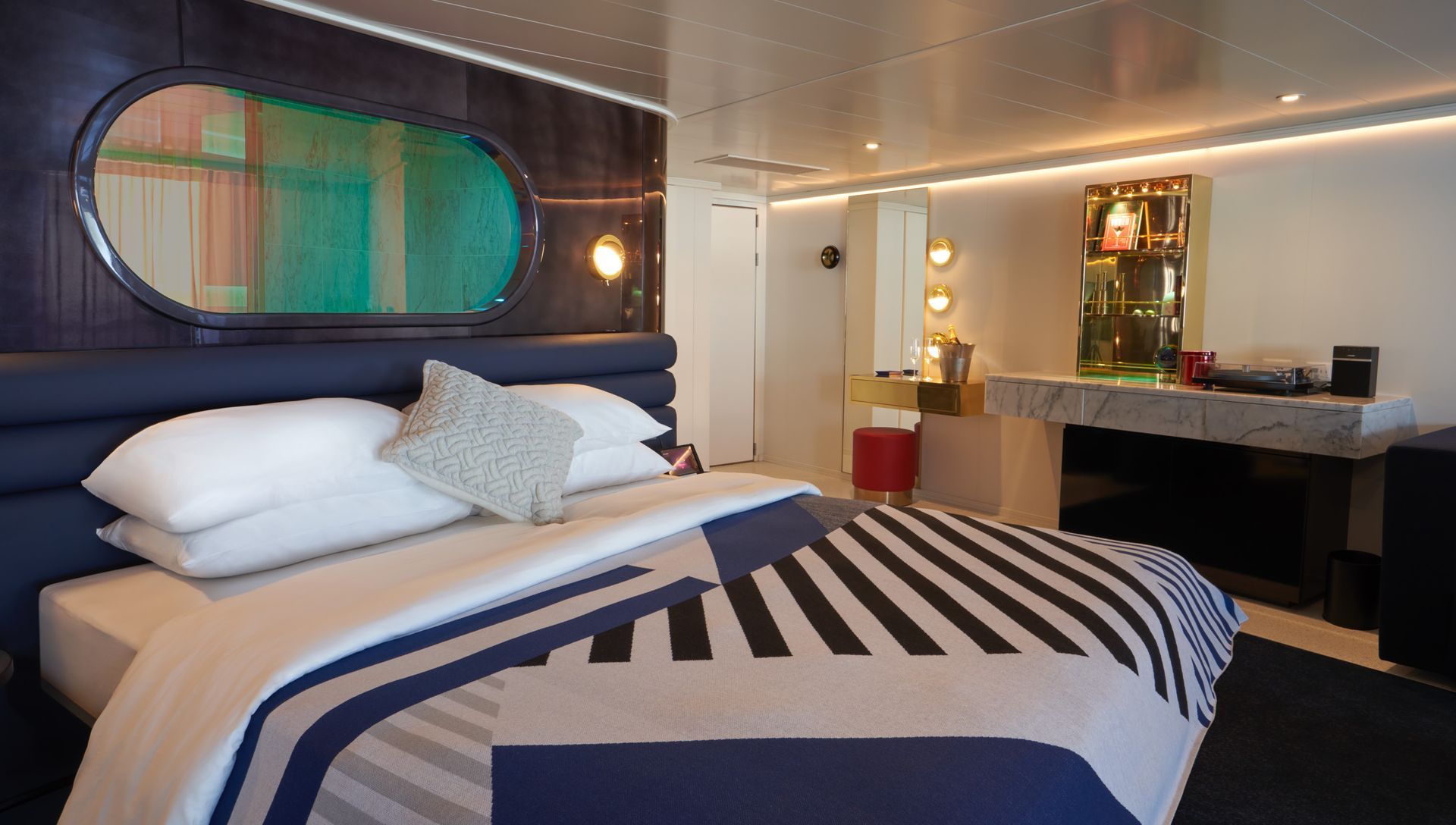 A modern cabin with a bed featuring blue and white patterned bedding. The room has a large window and a vanity.