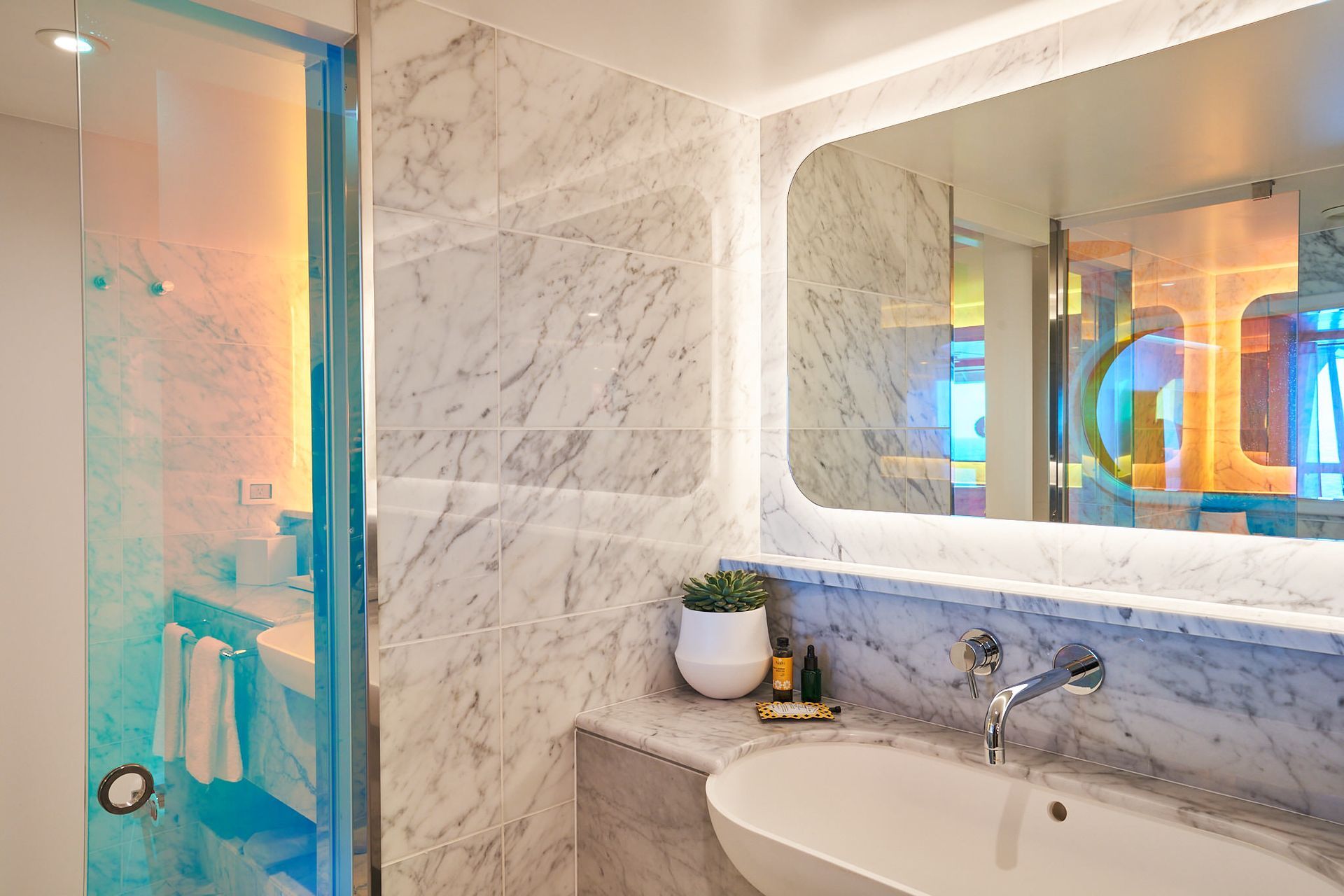 Modern bathroom with marble walls, oval sink, and a large mirror with a rainbow-hued glass shower.