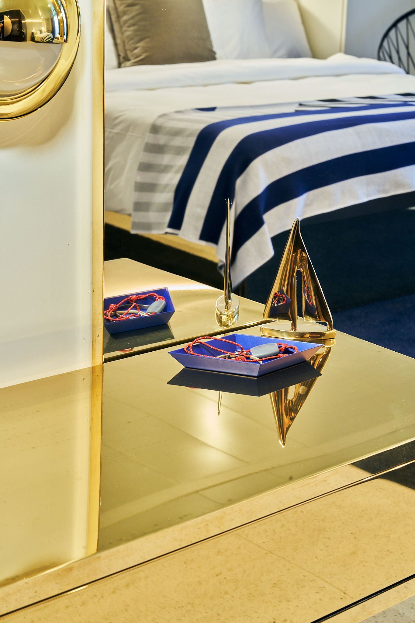 Mirror reflecting a bed with a blue and white striped blanket, plus a table with objects.