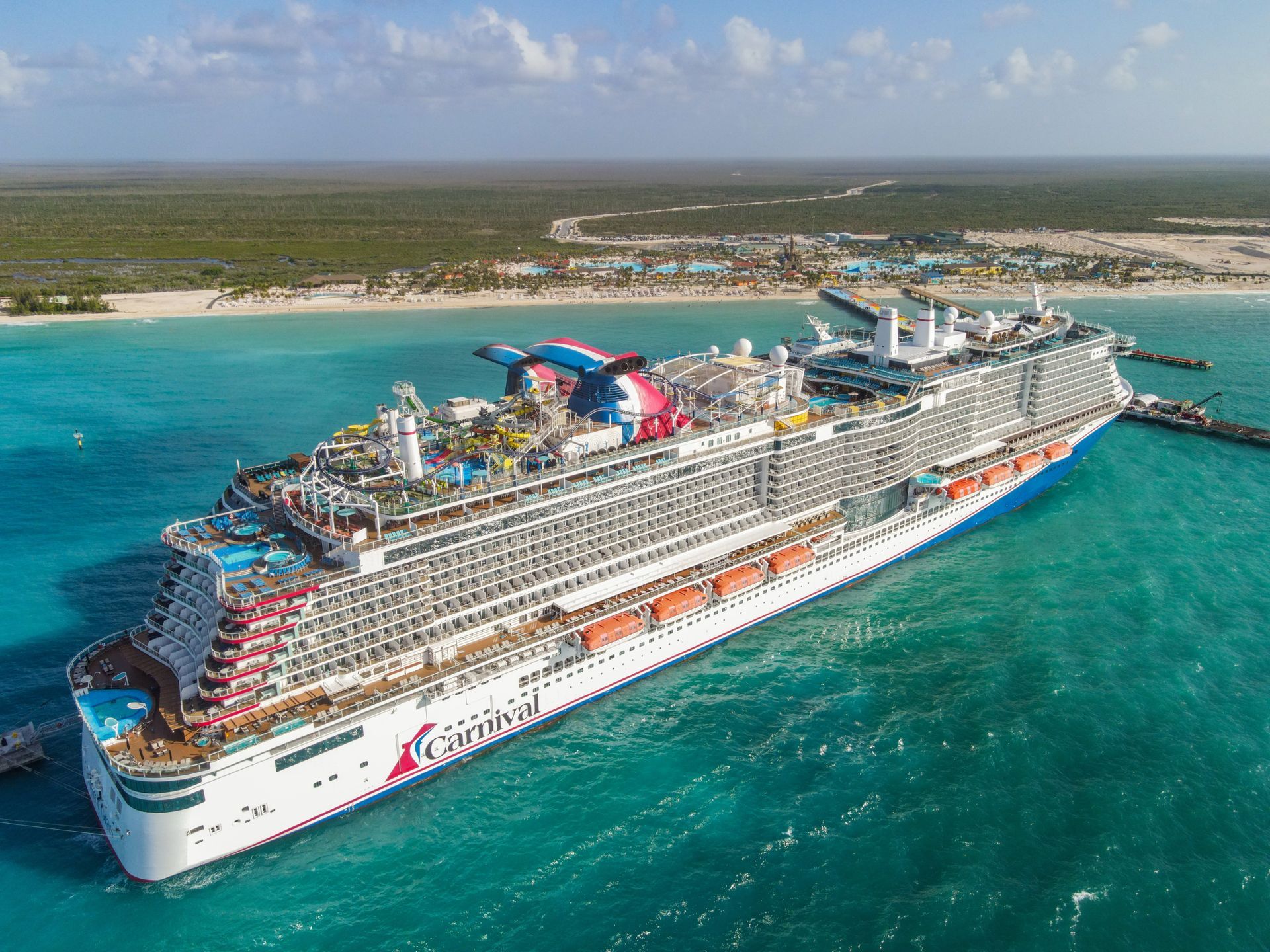 Large Carnival cruise ship docked at a tropical pier, turquoise water, blue sky.