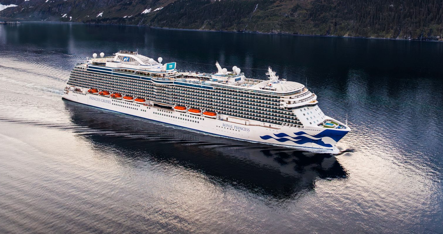 Cruise ship sailing on calm water near mountains.