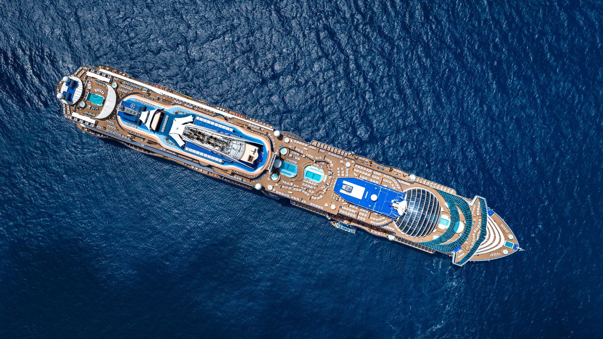 Overhead view of a cruise ship on blue water, featuring pools, decks, and structures.