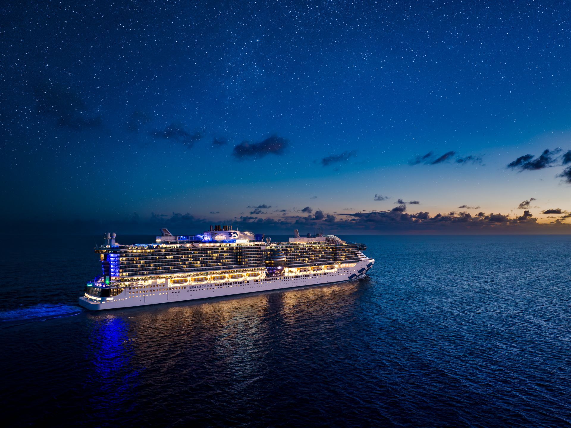 Cruise ship sailing on dark ocean under a starry night sky.