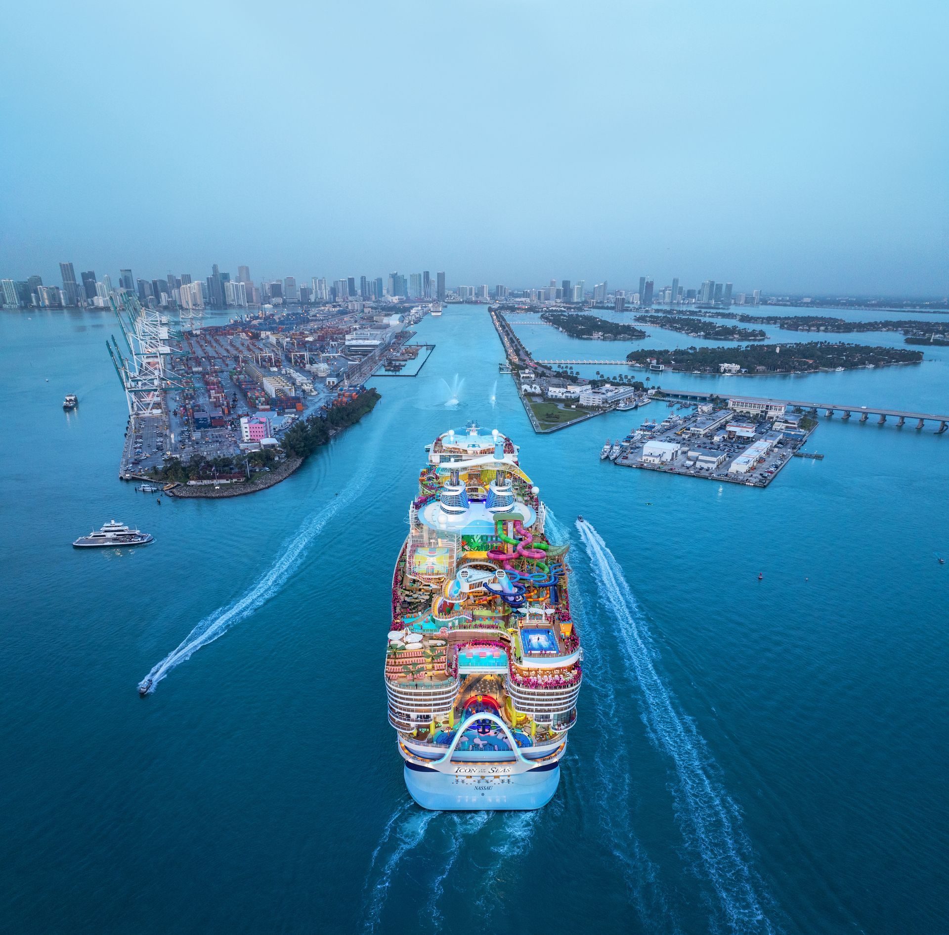 Cruise ship sailing through channel with cityscape and bridges in the background.