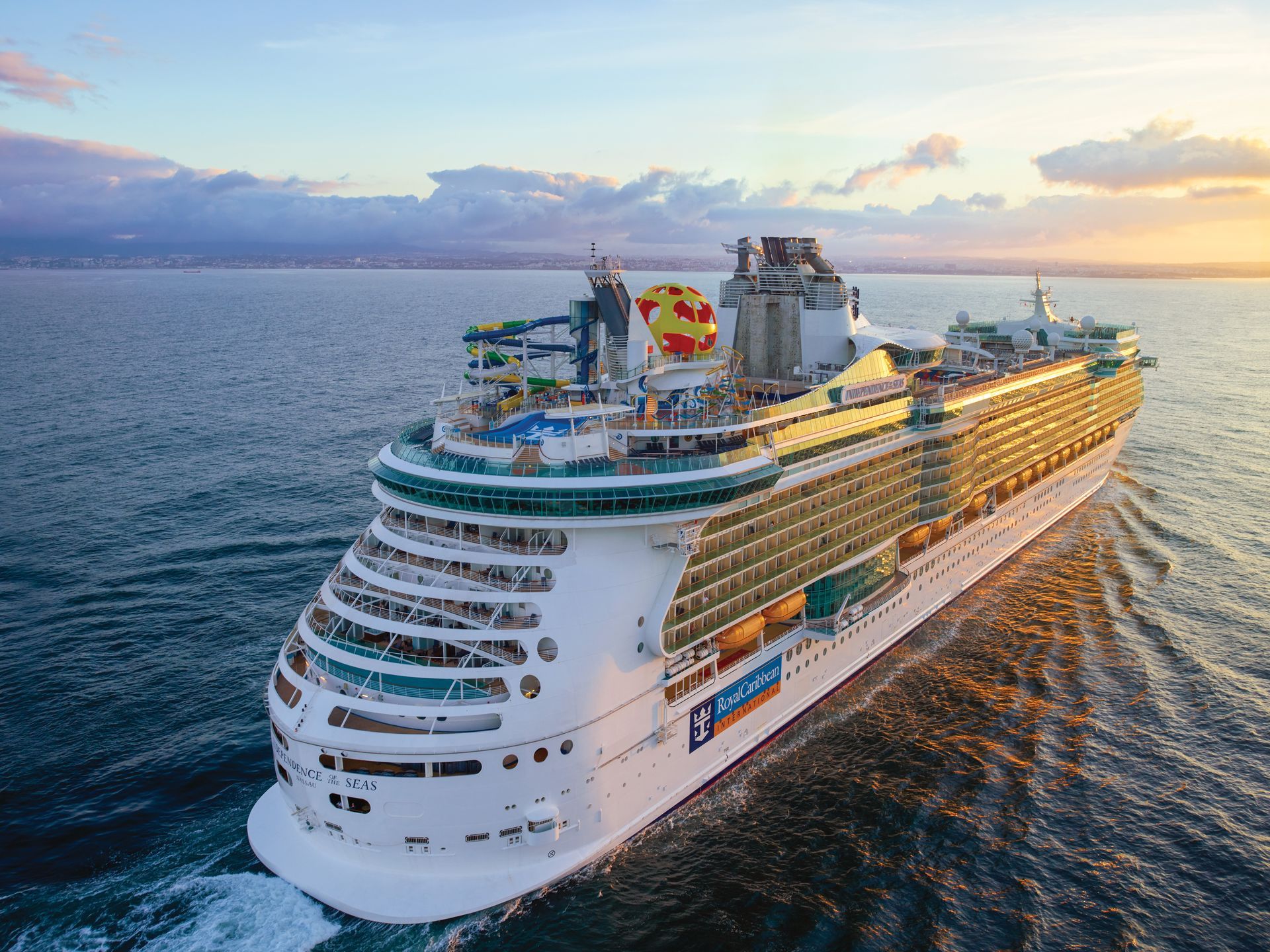 Cruise ship sailing on the ocean at sunset with water slides and decks.