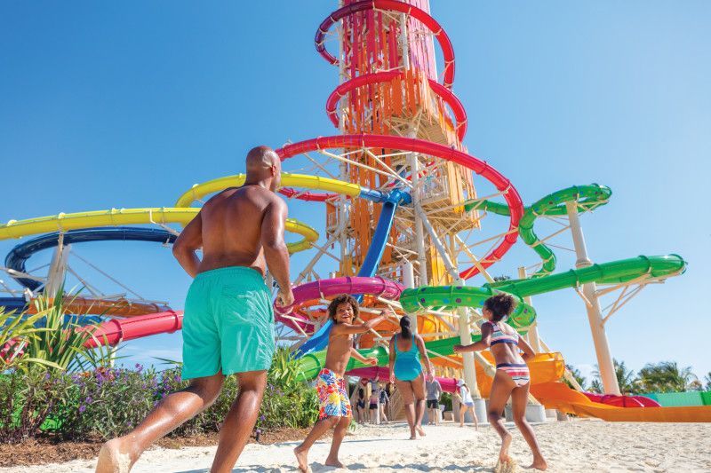 Family playing near colorful water slides and a tower under a blue sky.