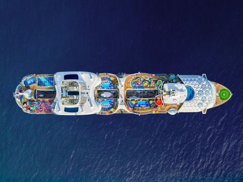 Overhead view of a large cruise ship on a blue sea, with various colorful decks and amenities visible.