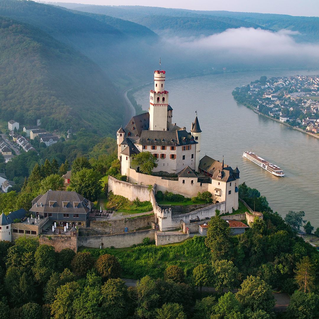 Medieval castle atop a hill overlooking a river; a cruise ship travels downstream.