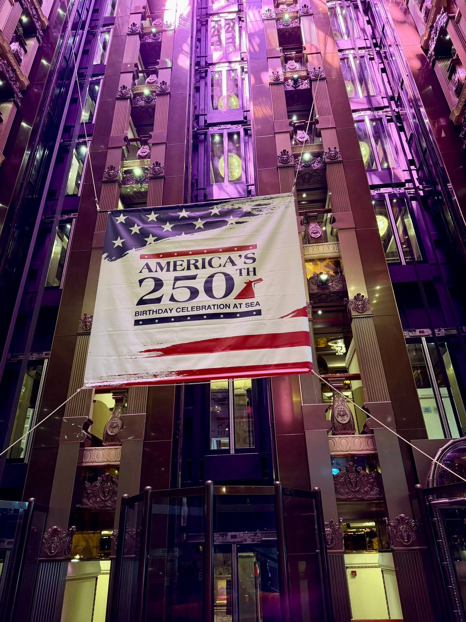 Banner reading “25 Years” hanging in a tall, purple-lit atrium with glass elevators