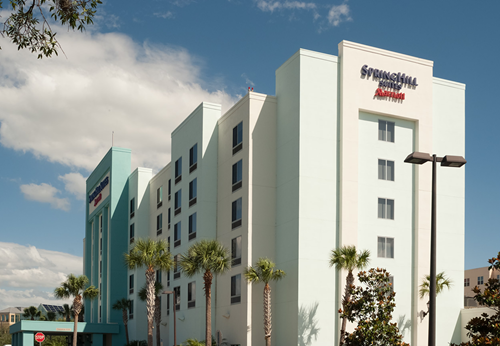 Modern hotel building with white and teal фасade, palm trees, and cloudy sky