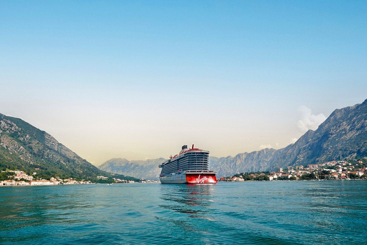 Cruise ship in a calm bay, flanked by mountains and a clear blue sky.