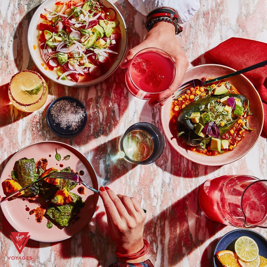 Overhead view of a colorful meal: hands holding drinks, plates of food, and colorful marble table.