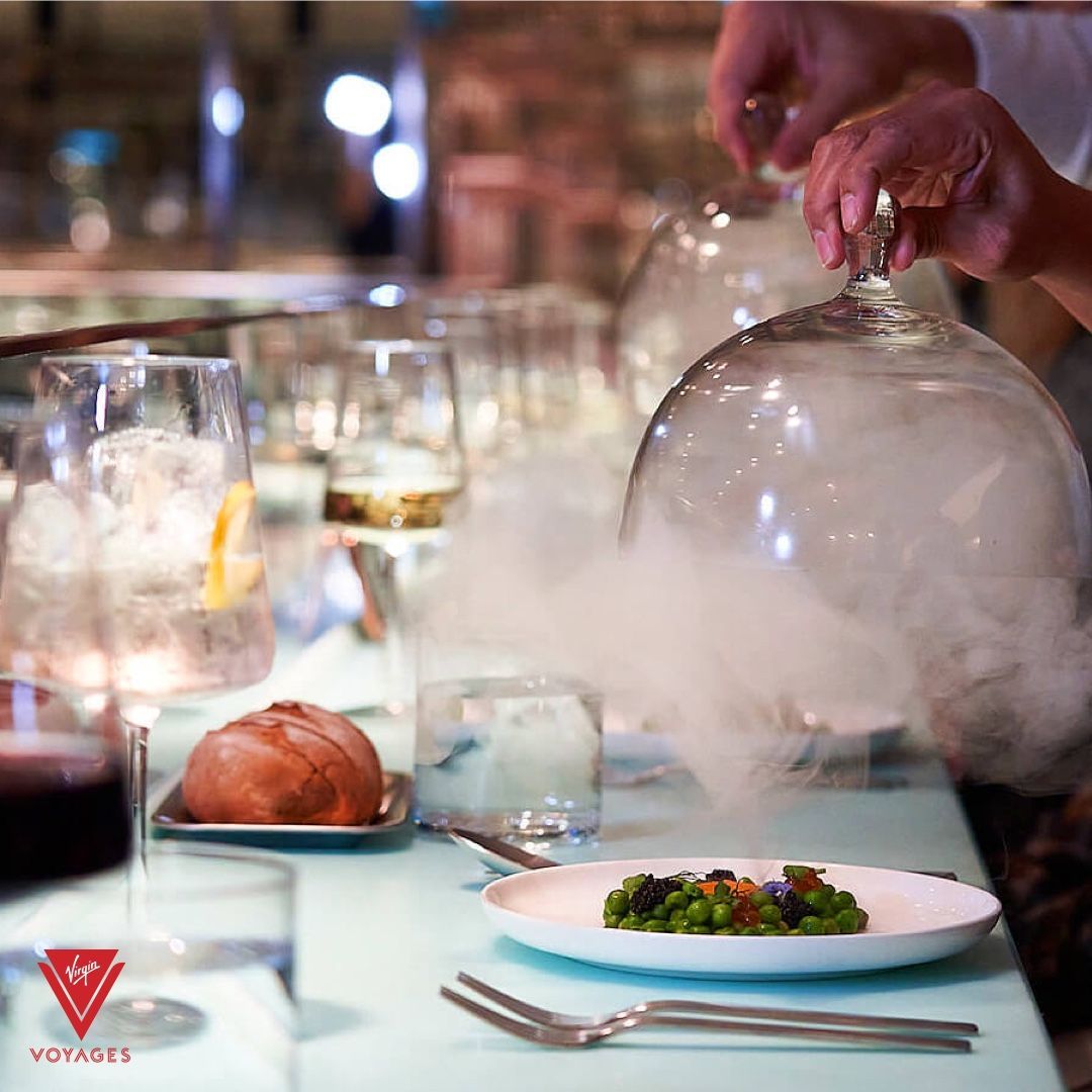 Table set for fine dining, food under a glass dome with smoke.