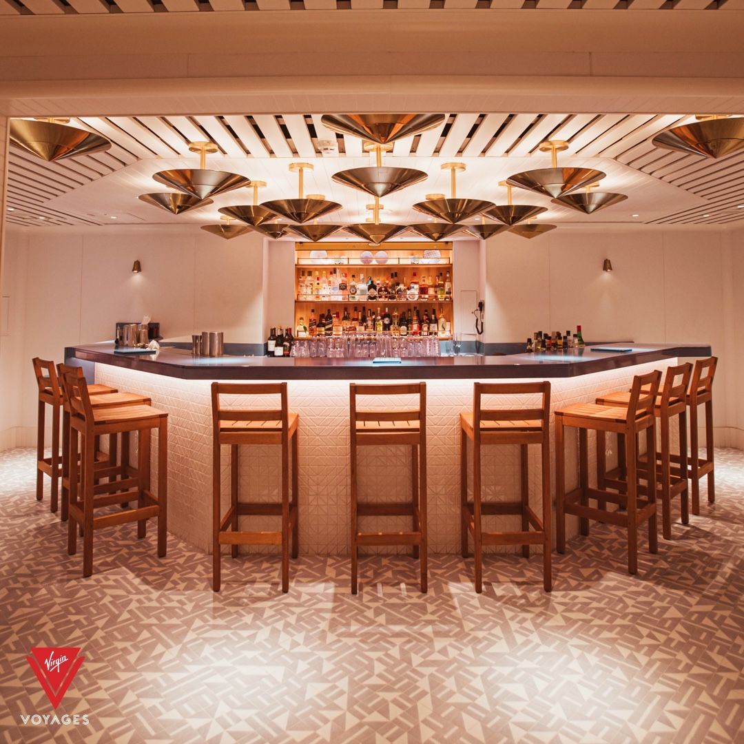 Bar with stools, overhead lighting, and bottles on a back shelf. Floor has a patterned design.