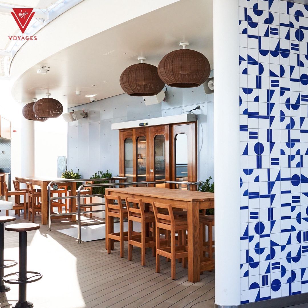 Outdoor bar with wood tables, chairs, and woven light fixtures; blue and white tiled wall.