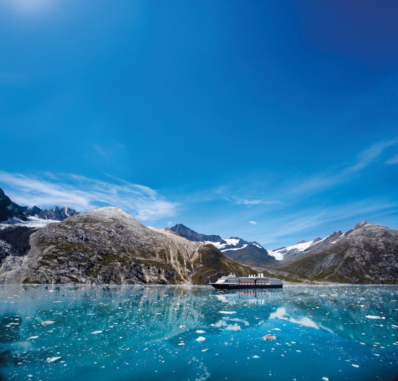 Cruise ship on turquoise water with glaciers and mountains under a blue sky.
