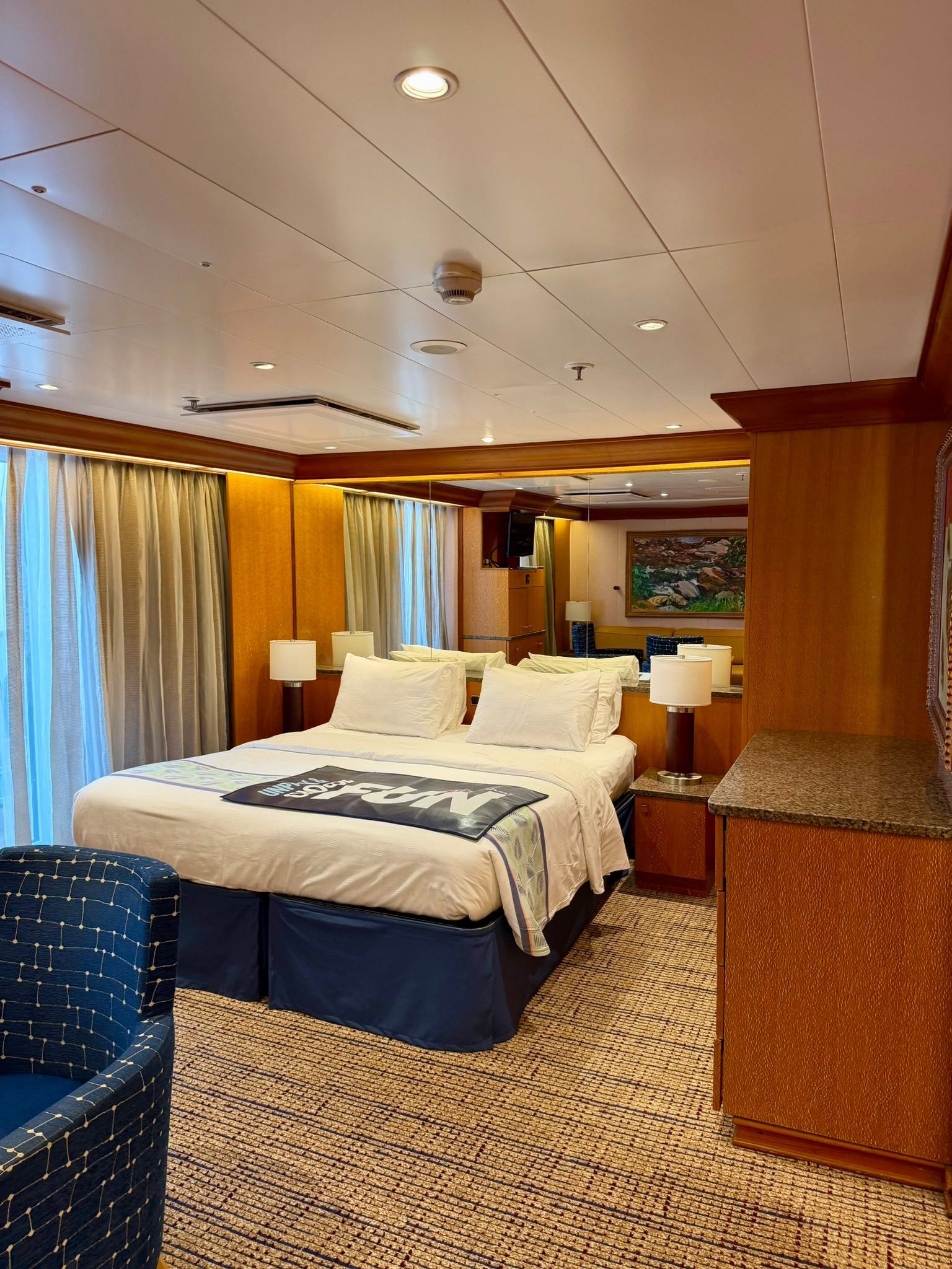 Hotel cabin-style bedroom with a neatly made bed, wood-paneled walls, and a large window with curtains.