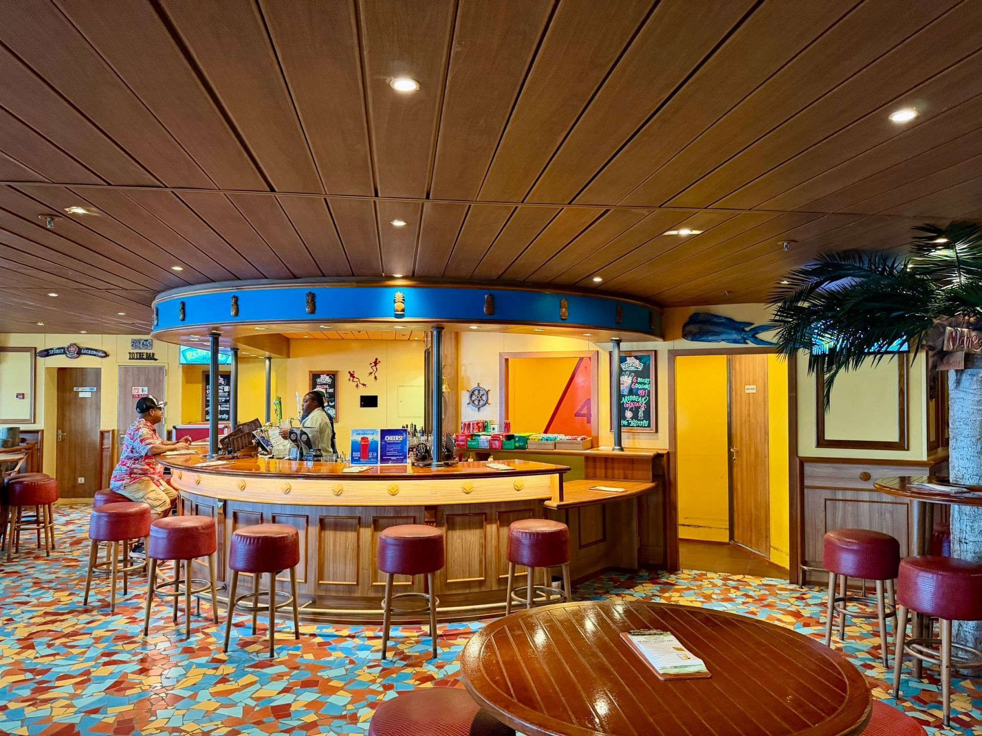 Colorful restaurant lounge with curved wooden bar, red stools, patterned floor, and warm ceiling lights
