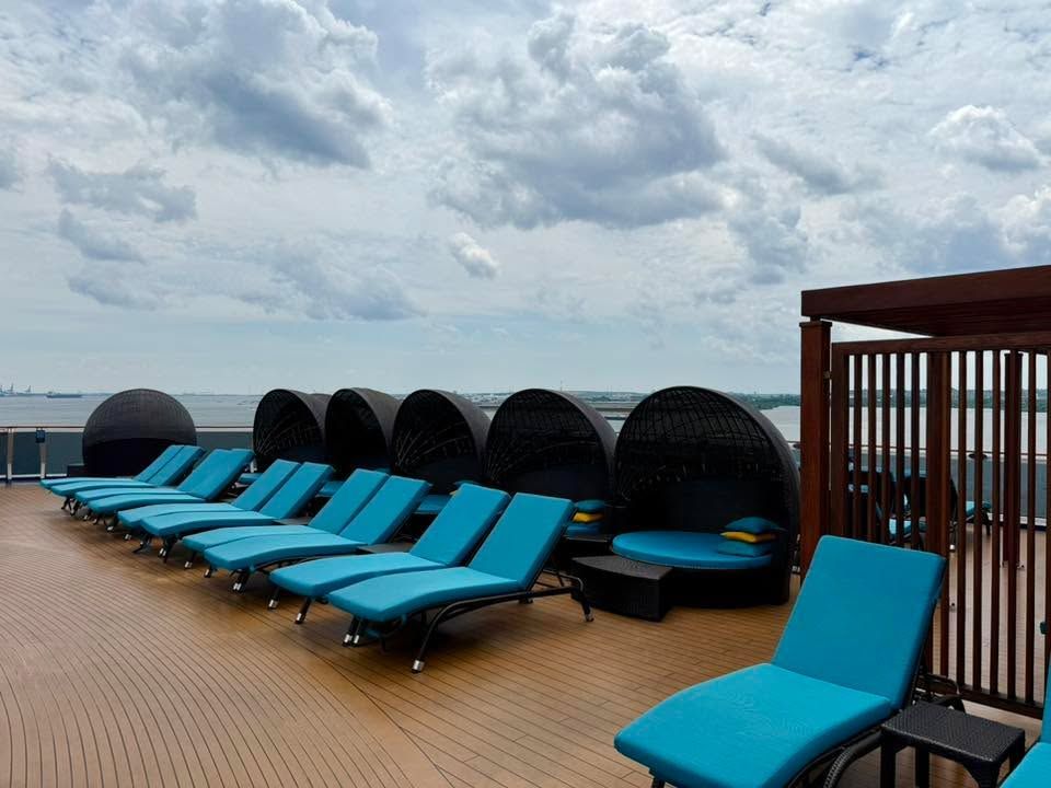 Blue lounge chairs on a rooftop deck overlooking the sea under a cloudy sky