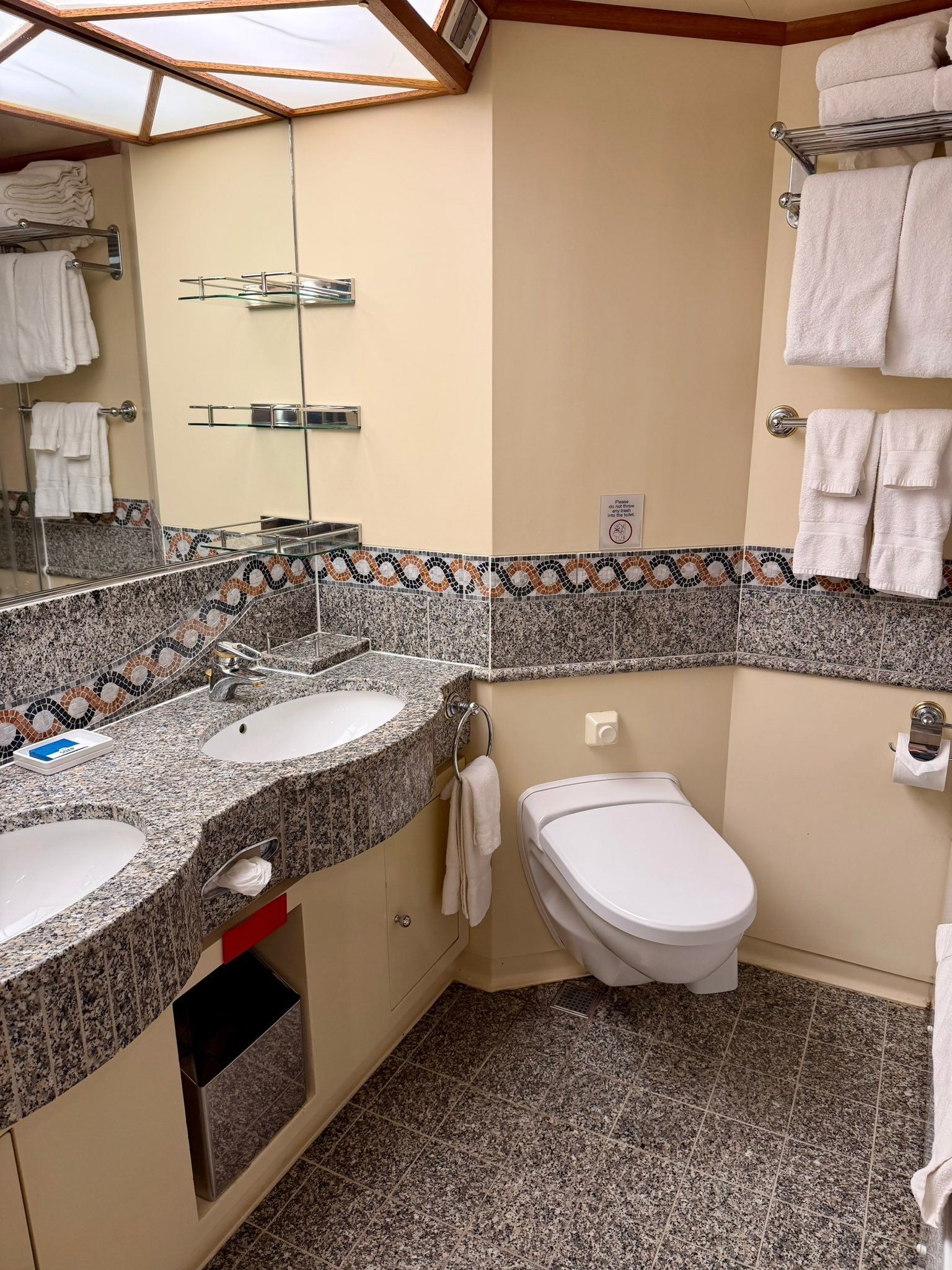 Spacious bathroom with beige walls, granite counters, twin sinks, toilet, and large mirror with shelves.