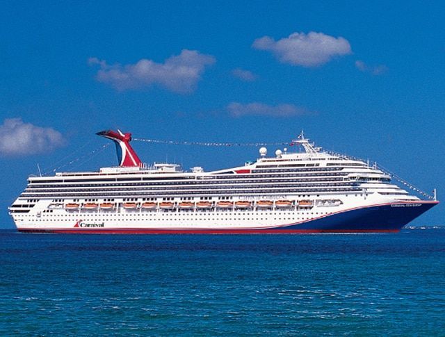Cruise ship sailing on blue ocean under a bright blue sky with white clouds.