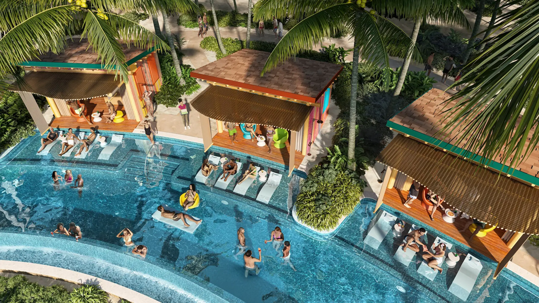 Aerial view of a resort pool with swimmers, lounge chairs, and colorful tiki huts.