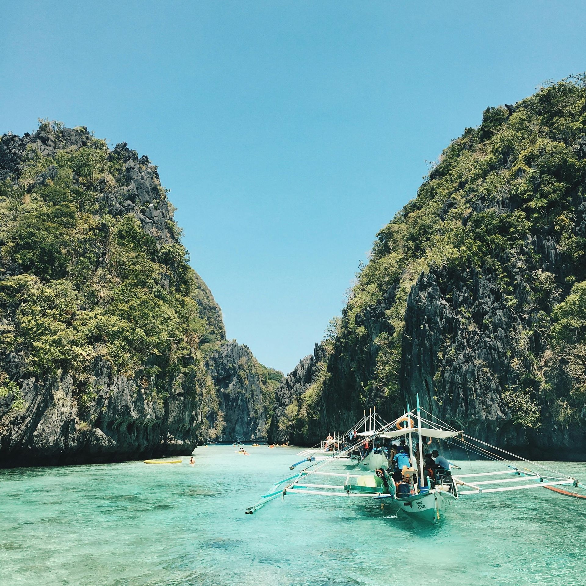 Boat in turquoise water between lush, rocky cliffs under a clear blue sky.