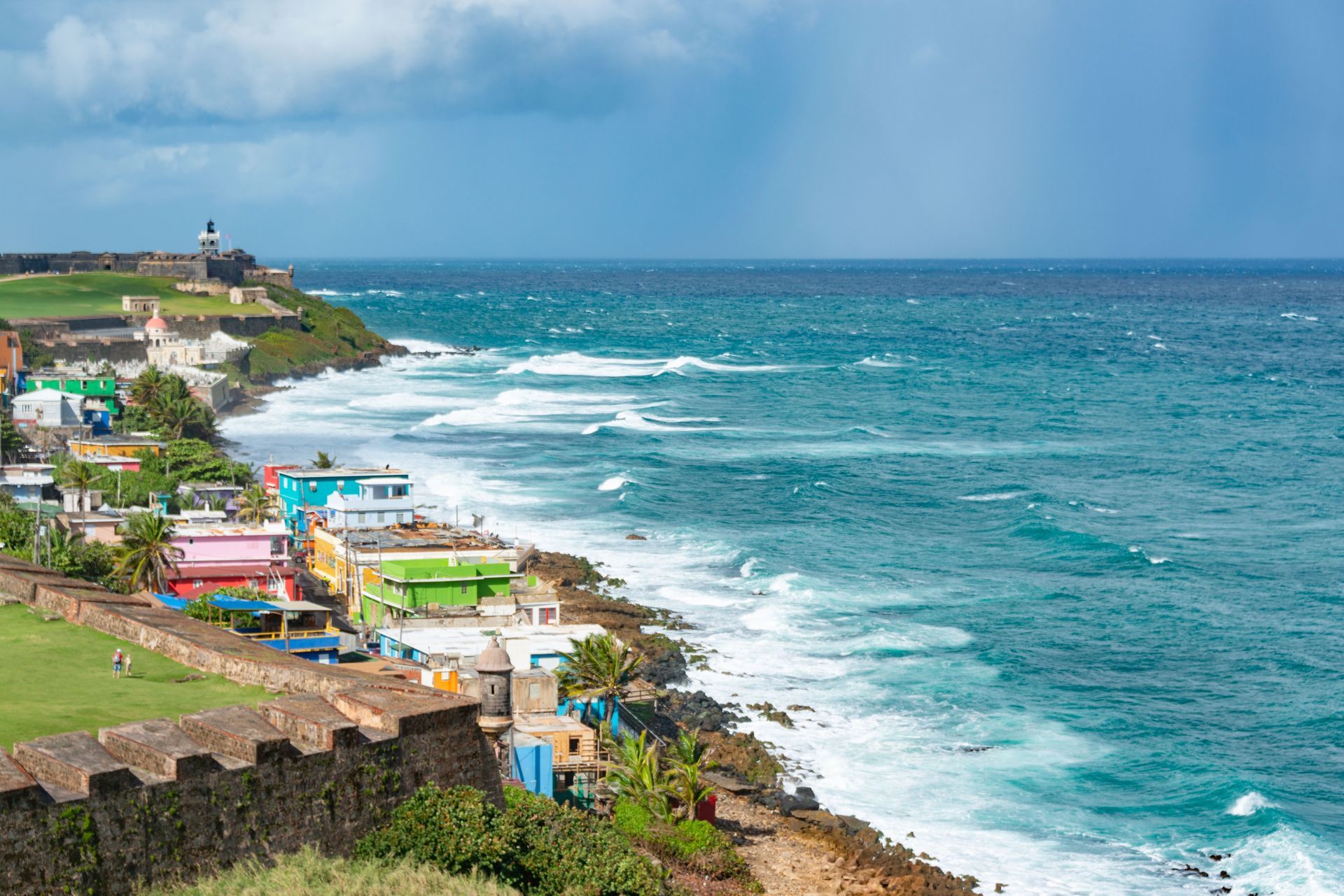 Colorful seaside village along a rocky coast with turquoise ocean waves and a distant lighthouse