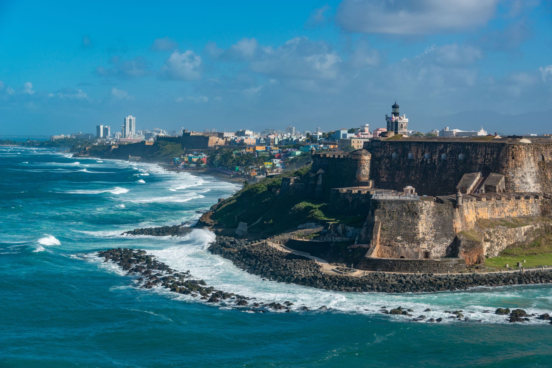 Coastal fortress above turquoise waves with a city skyline in the distance