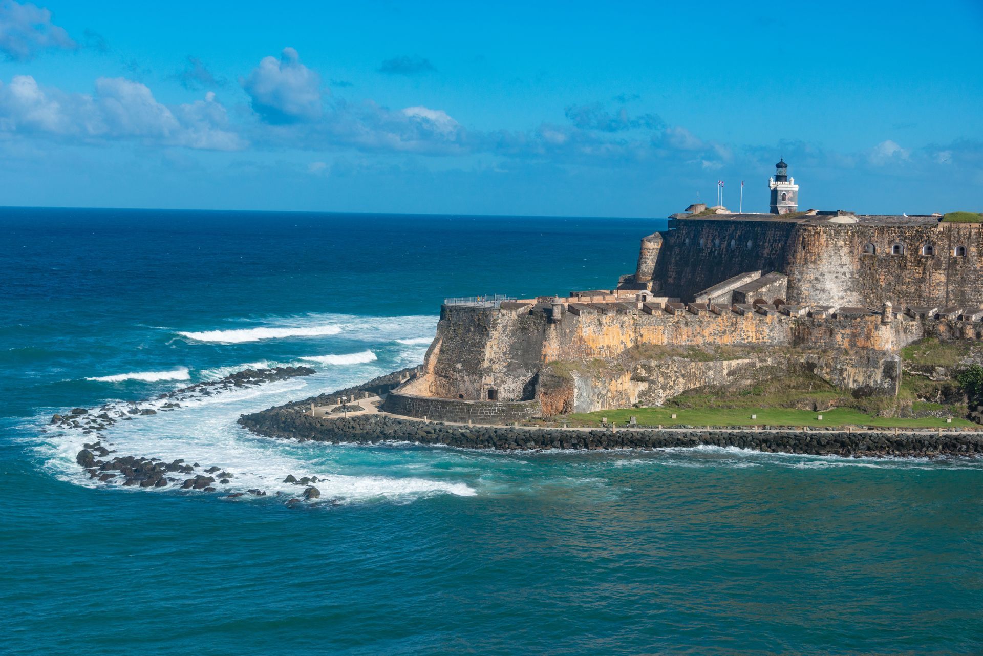 Coastal fort on rocky cliffs above turquoise ocean with white waves and blue sky