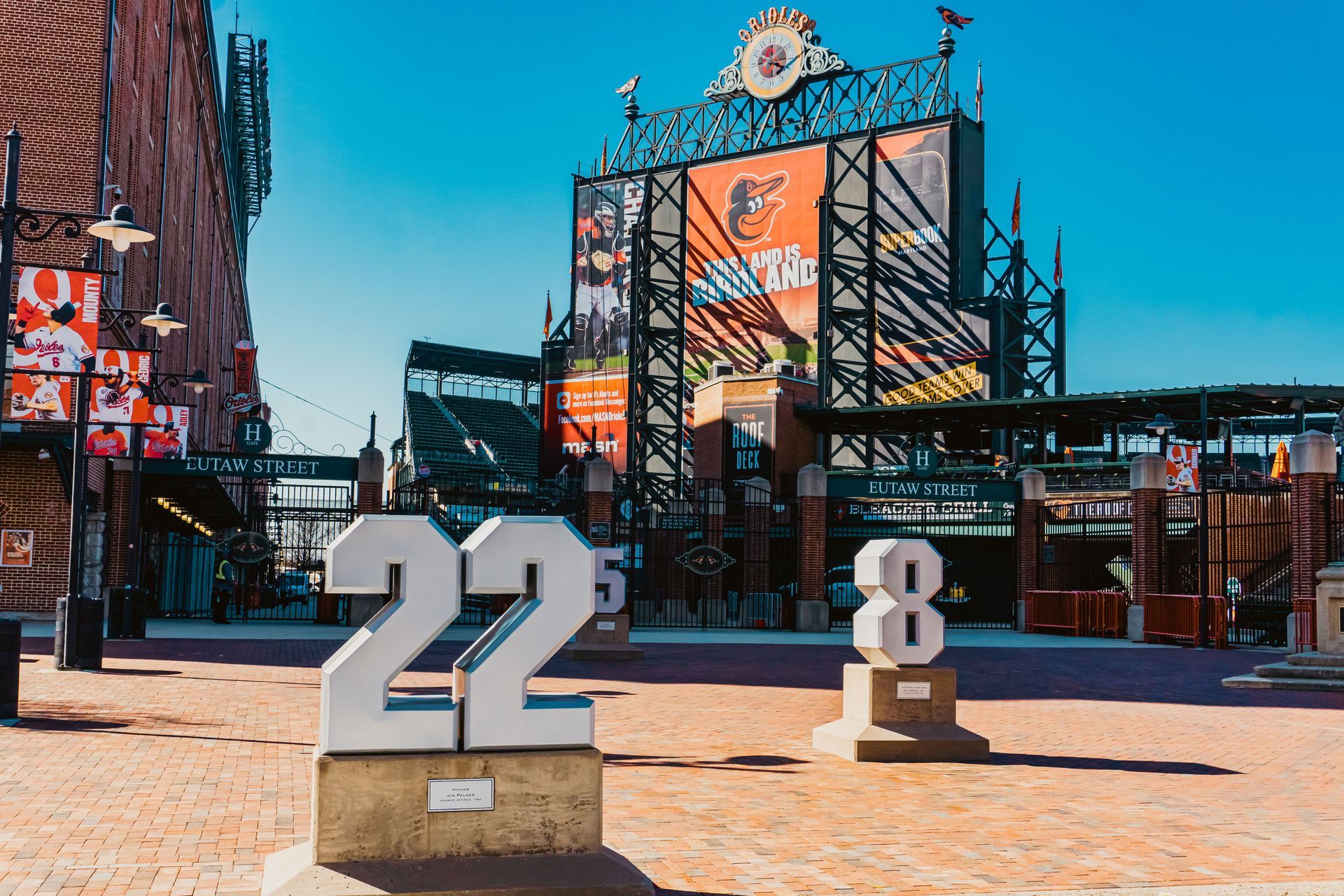 Two large number sculptures, 22 and 8, in front of a colorful stadium entrance under a blue sky