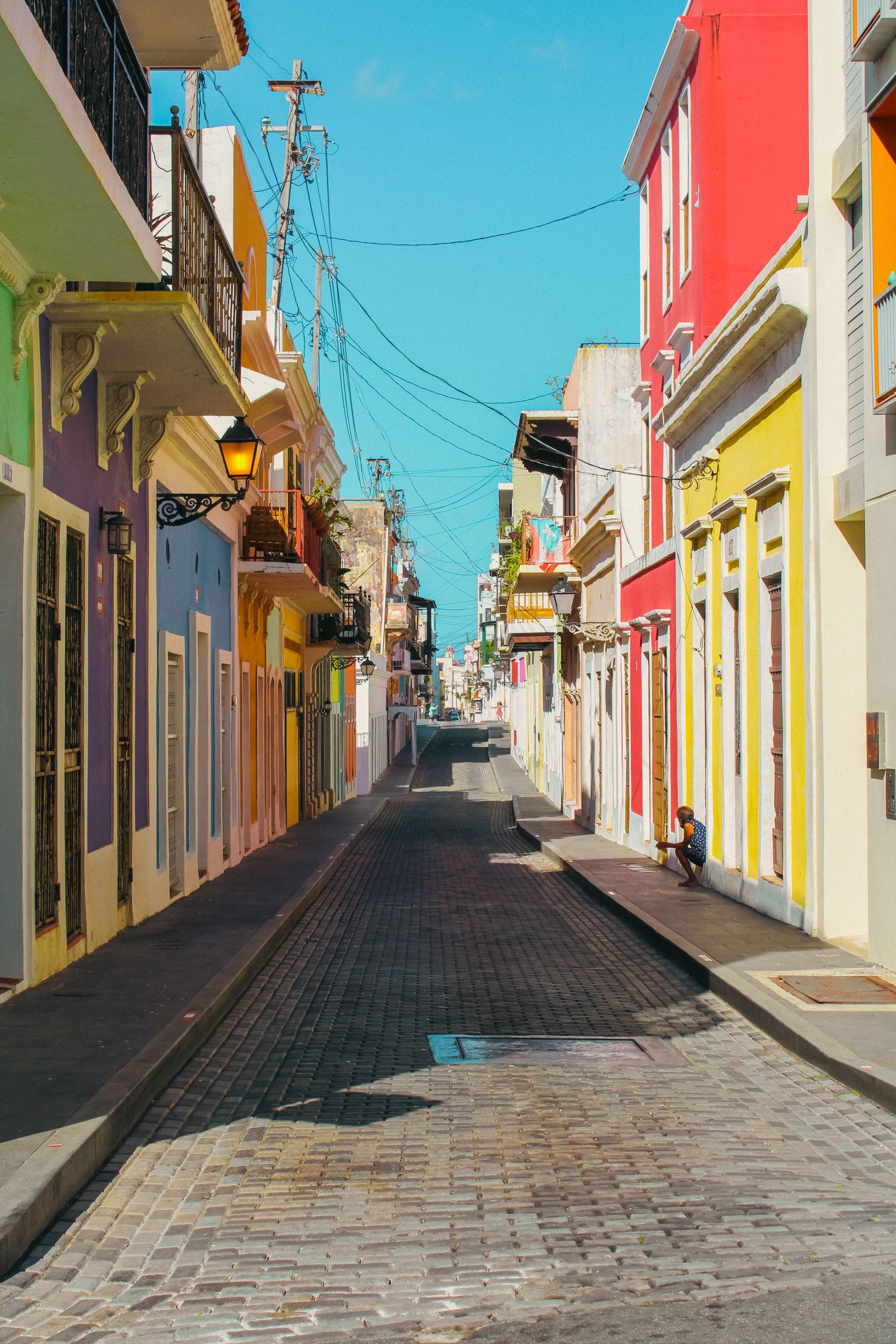 Colorful narrow cobblestone street lined with bright buildings under a clear blue sky