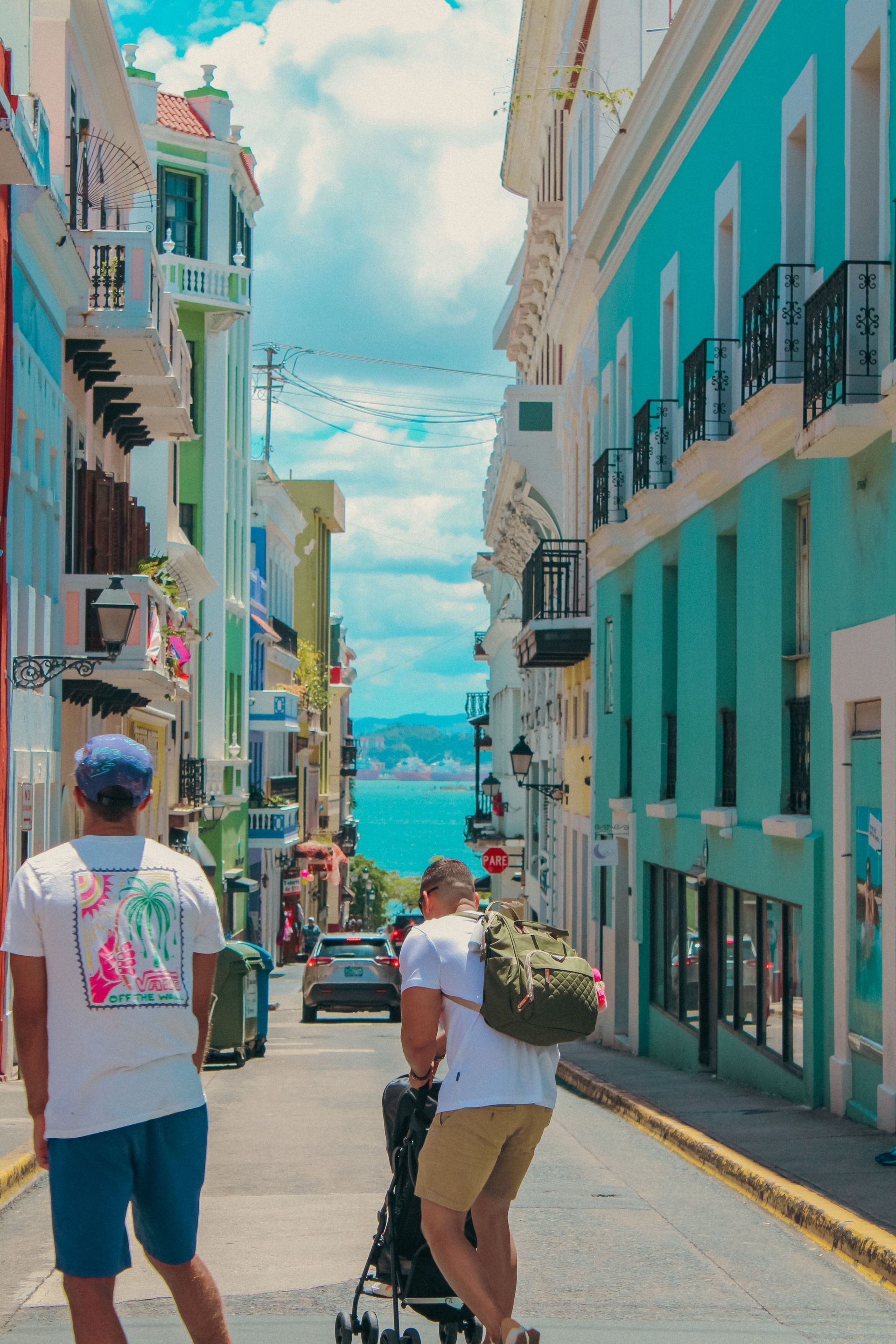 Two people walking down a colorful, steep street toward the sea
