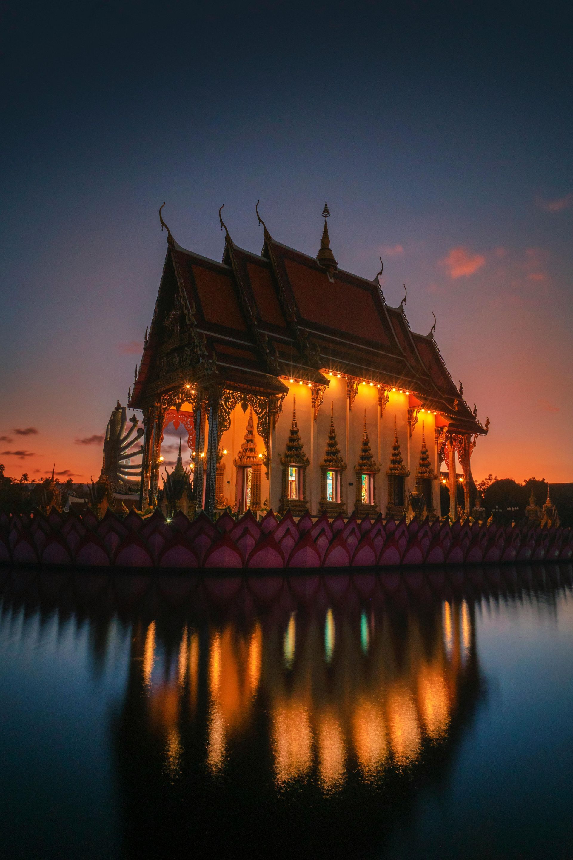 Temple at sunset, reflected in water; orange and blue sky, illuminated building.