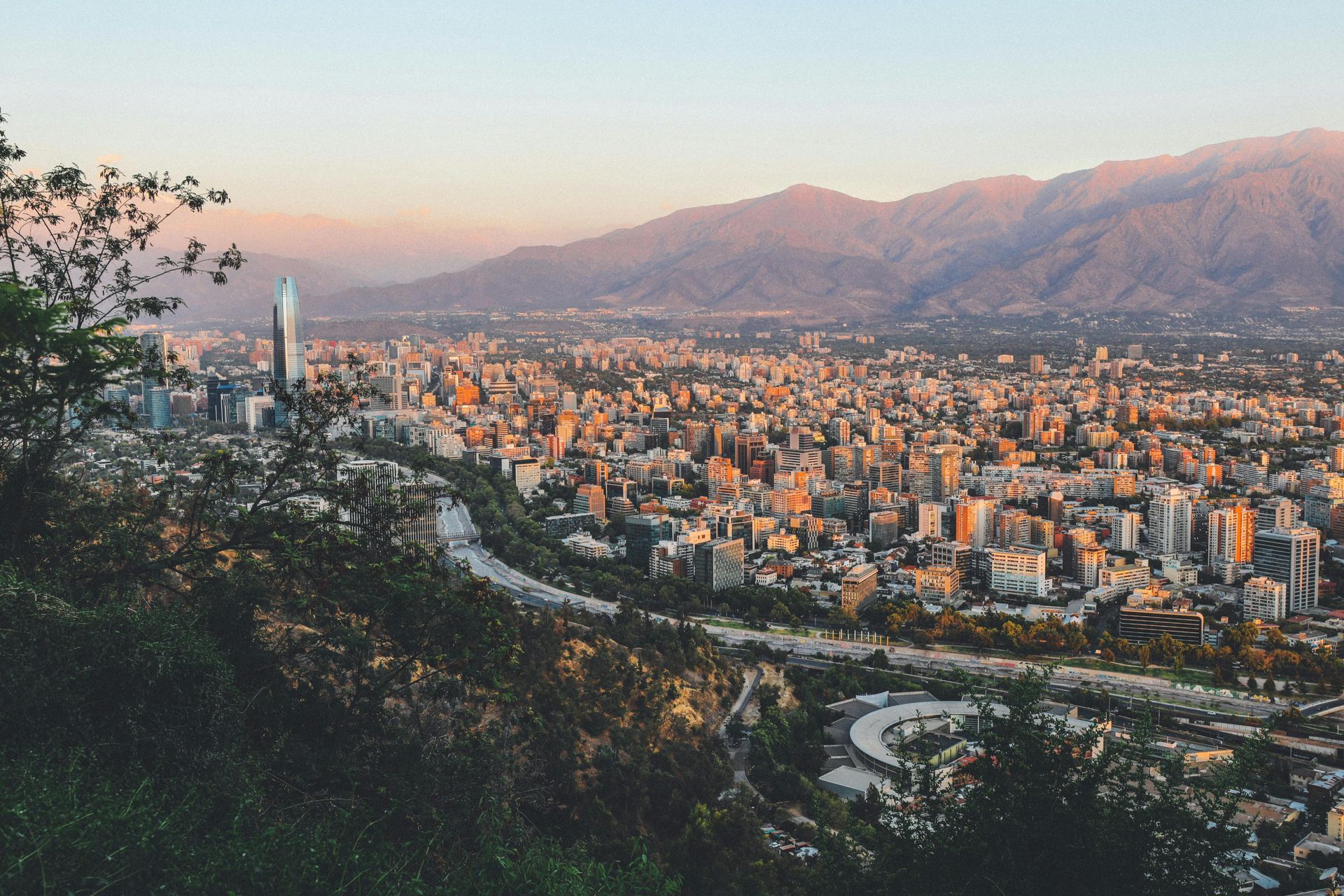 Cityscape of Santiago, Chile, with mountains in the background, bathed in the warm light of sunrise or sunset.