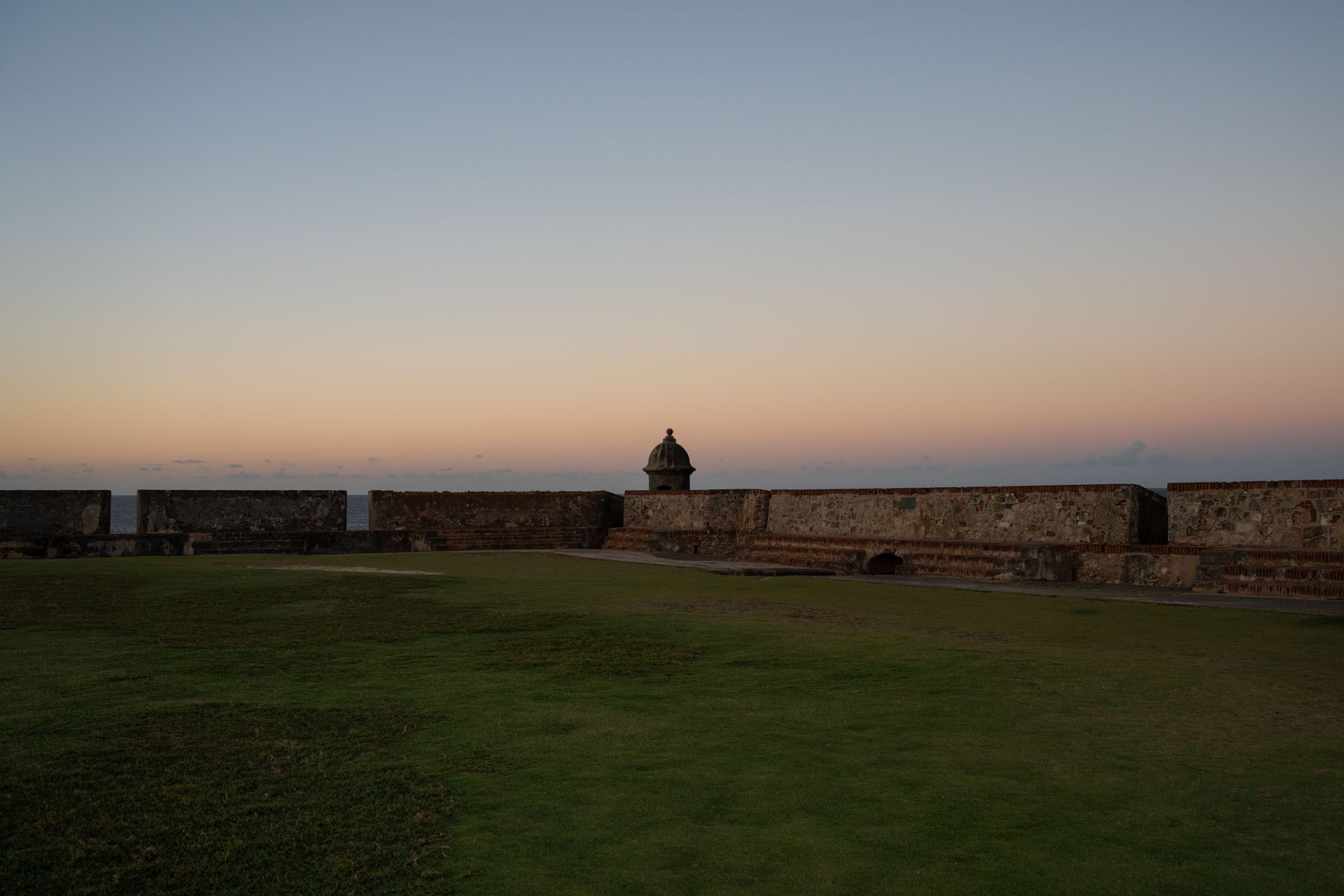 Stone fort wall at dusk above a grassy field under a fading blue-orange sky