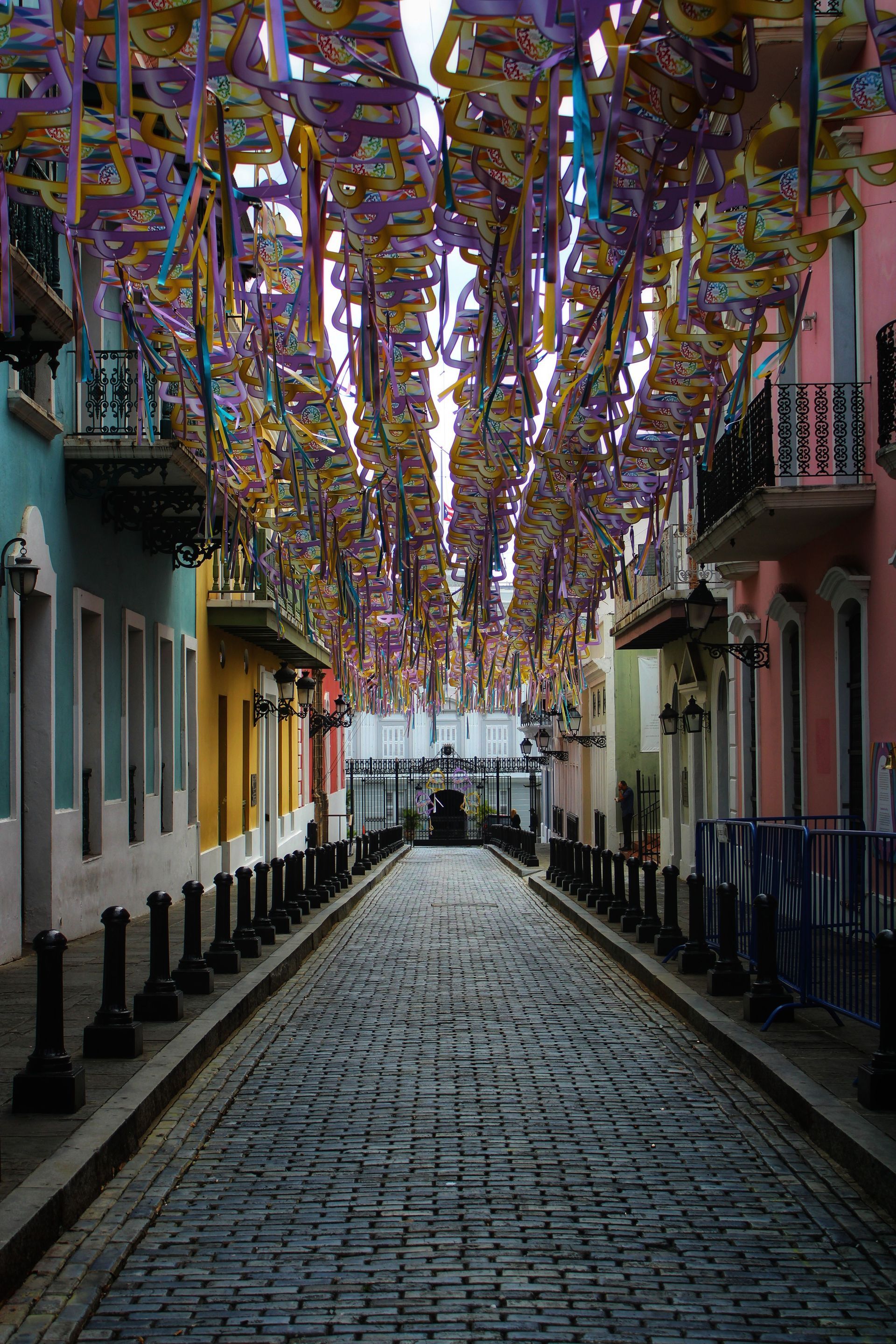Narrow cobblestone street lined with colorful buildings and hanging purple-and-gold decorations overhead