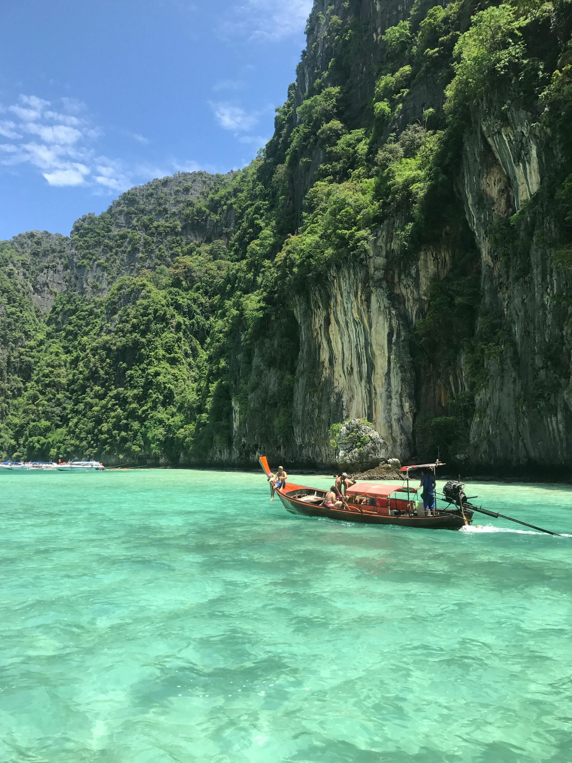 Boat on turquoise water near a limestone cliff covered in lush green vegetation under a blue sky.