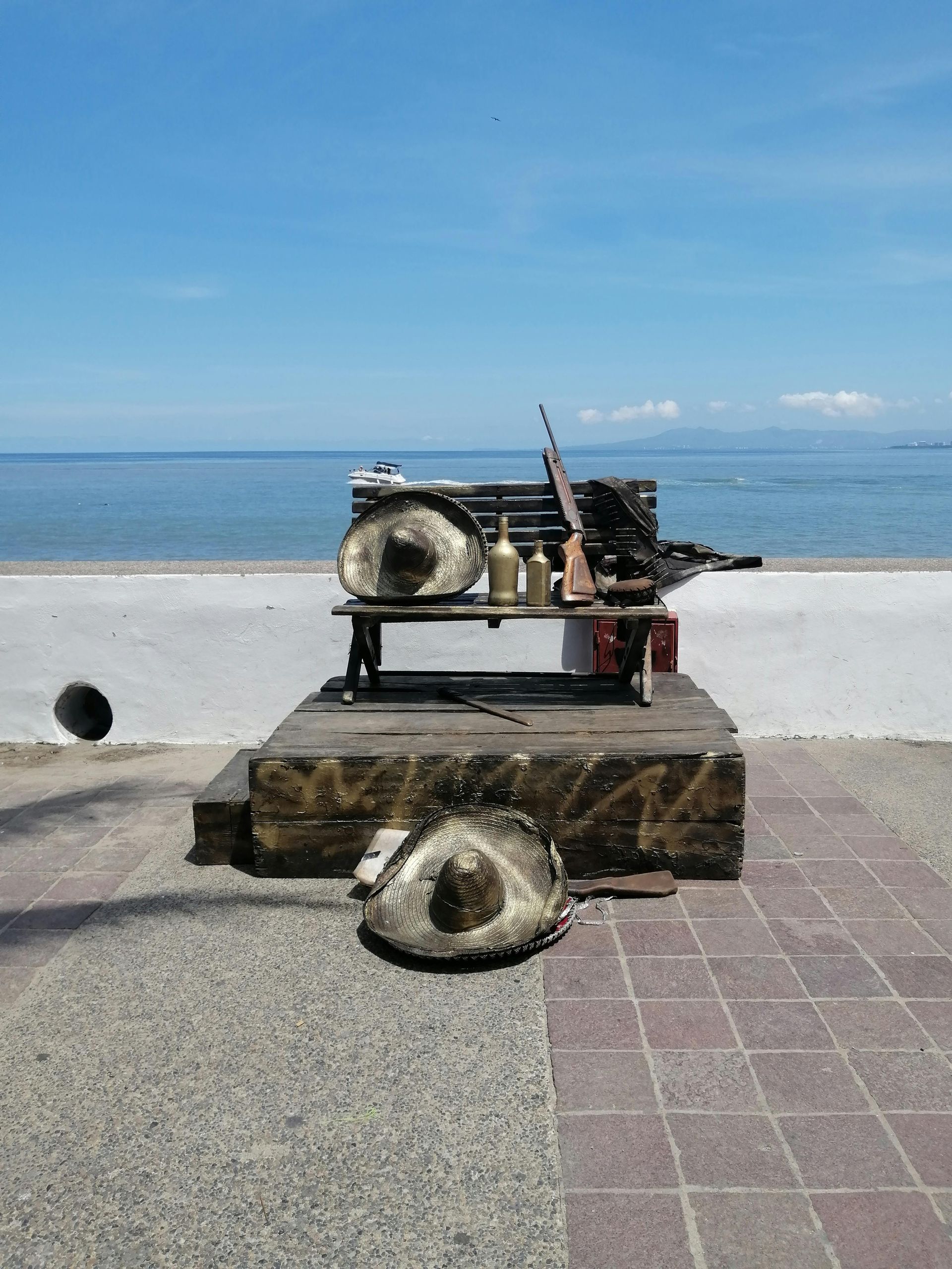 Rusting mechanical sculpture on a seaside promenade with ocean and blue sky behind.