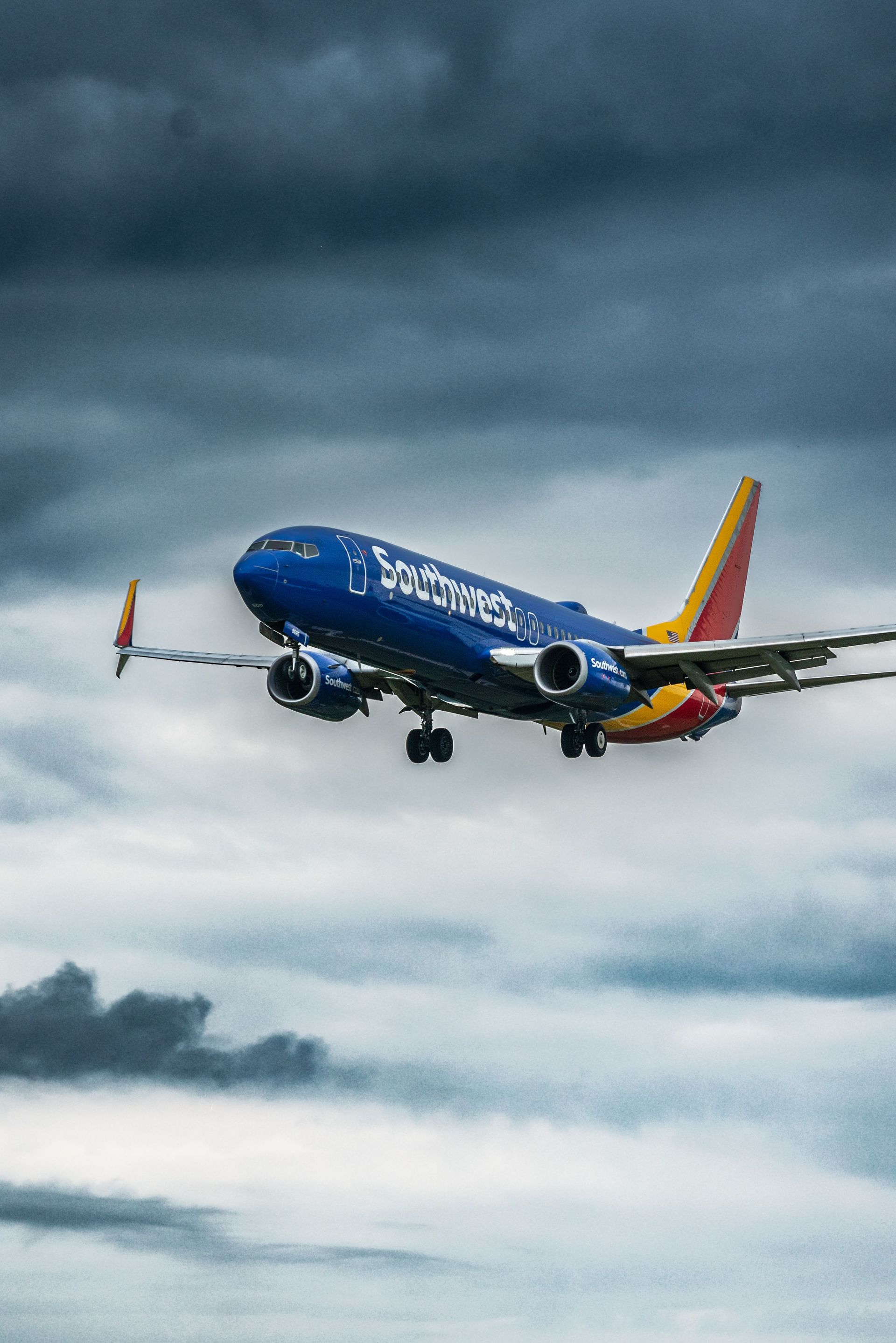 Blue and red passenger jet flying low against a cloudy sky