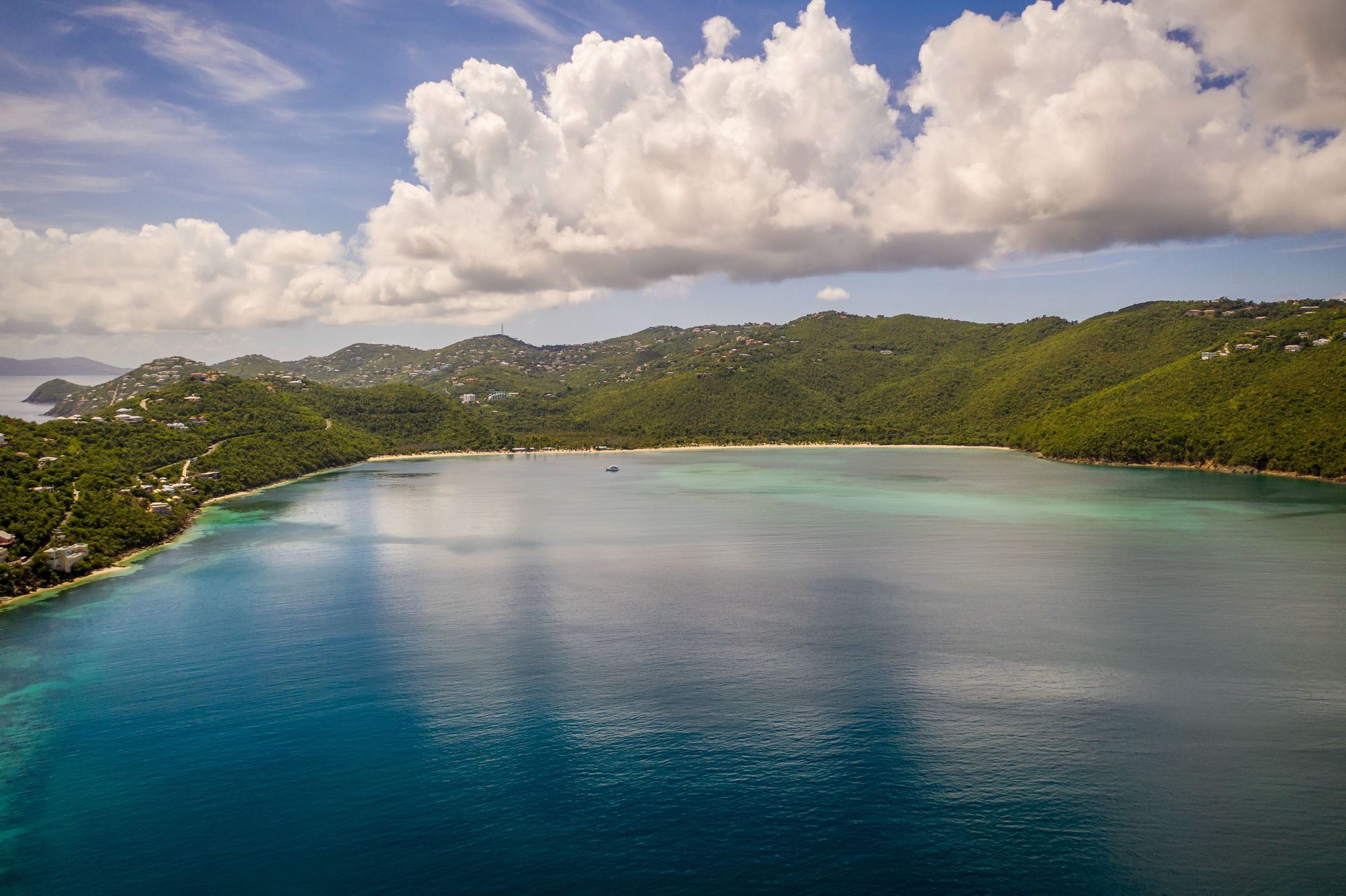 Tropical bay with turquoise water, green hills, and large white clouds under a blue sky
