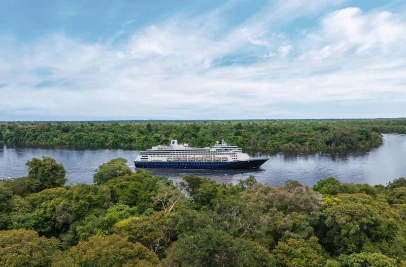 A cruise ship that is white and blue sailing up the Amazon river and is surrounded by the forest.