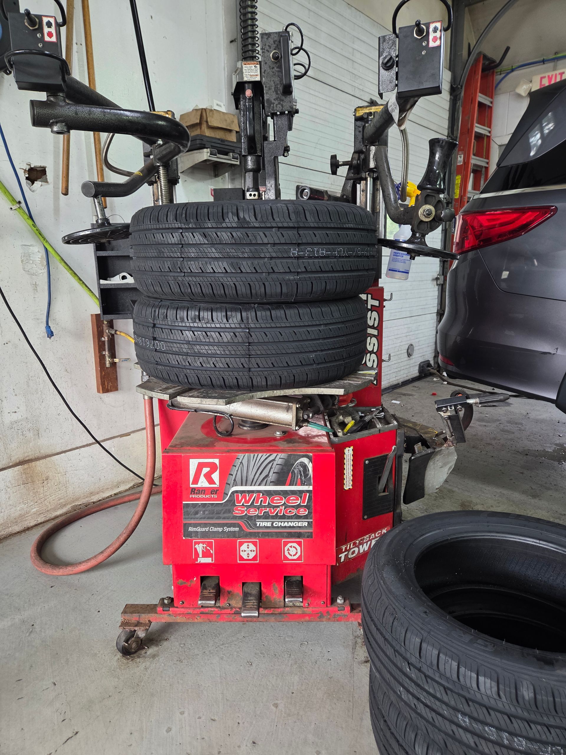 Car tires stacked on a red tire-changing machine in an auto shop garage. | Suburban Wrench